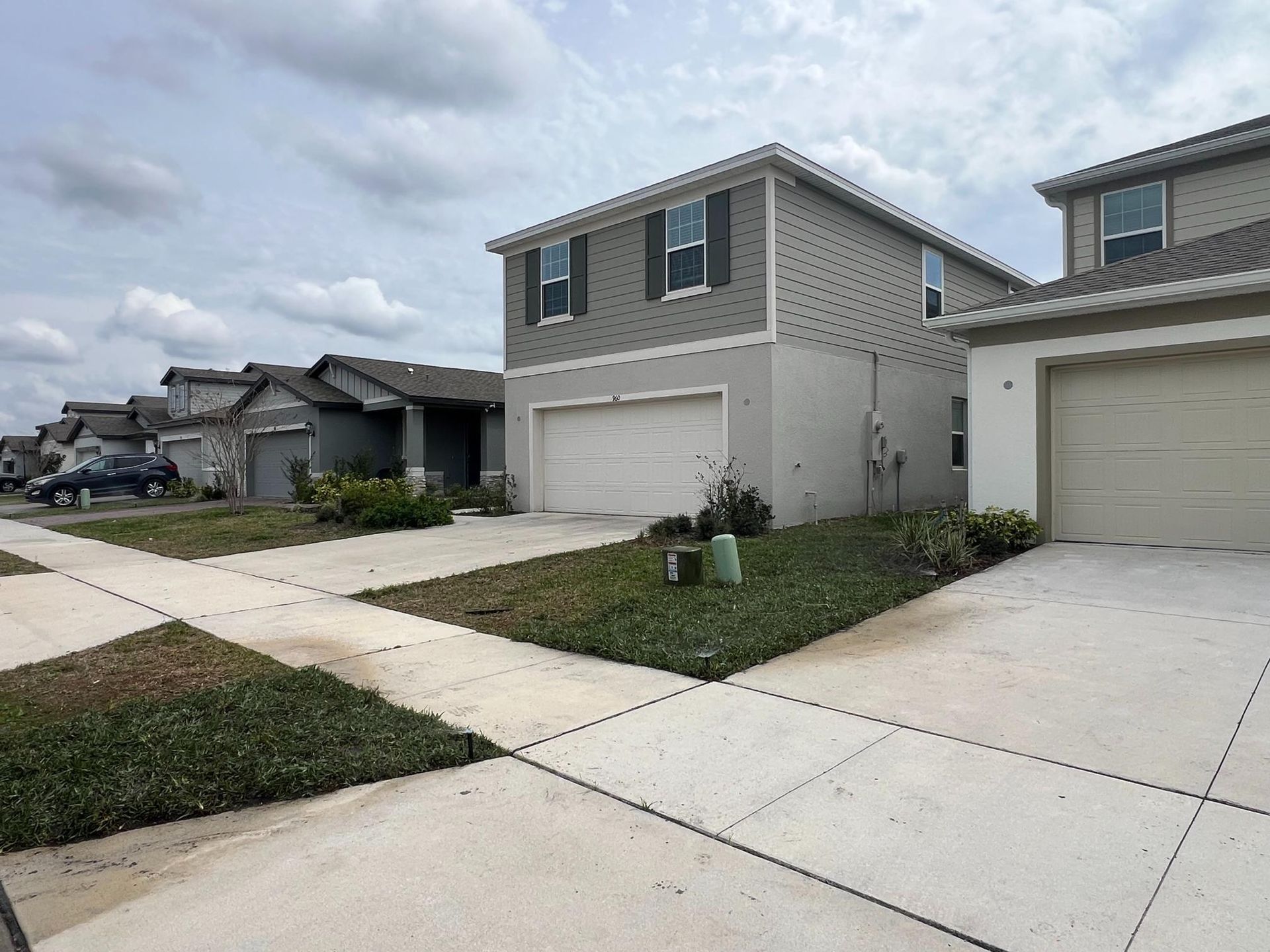 Row of modern two-story houses with driveways, sidewalks, and green lawns under a cloudy sky.