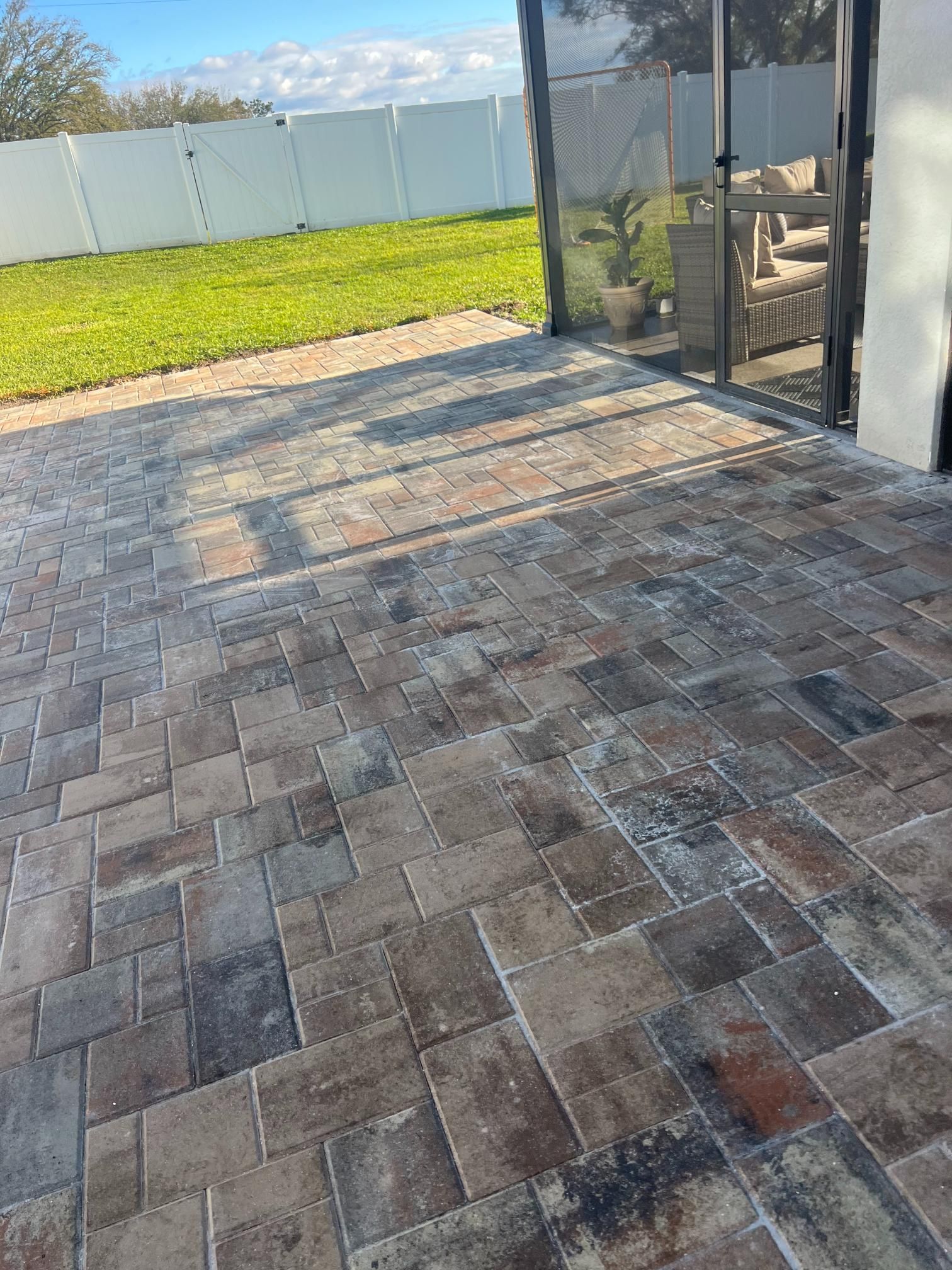Brick patio with varied shades of brown, overlooking a grassy lawn and white fence.