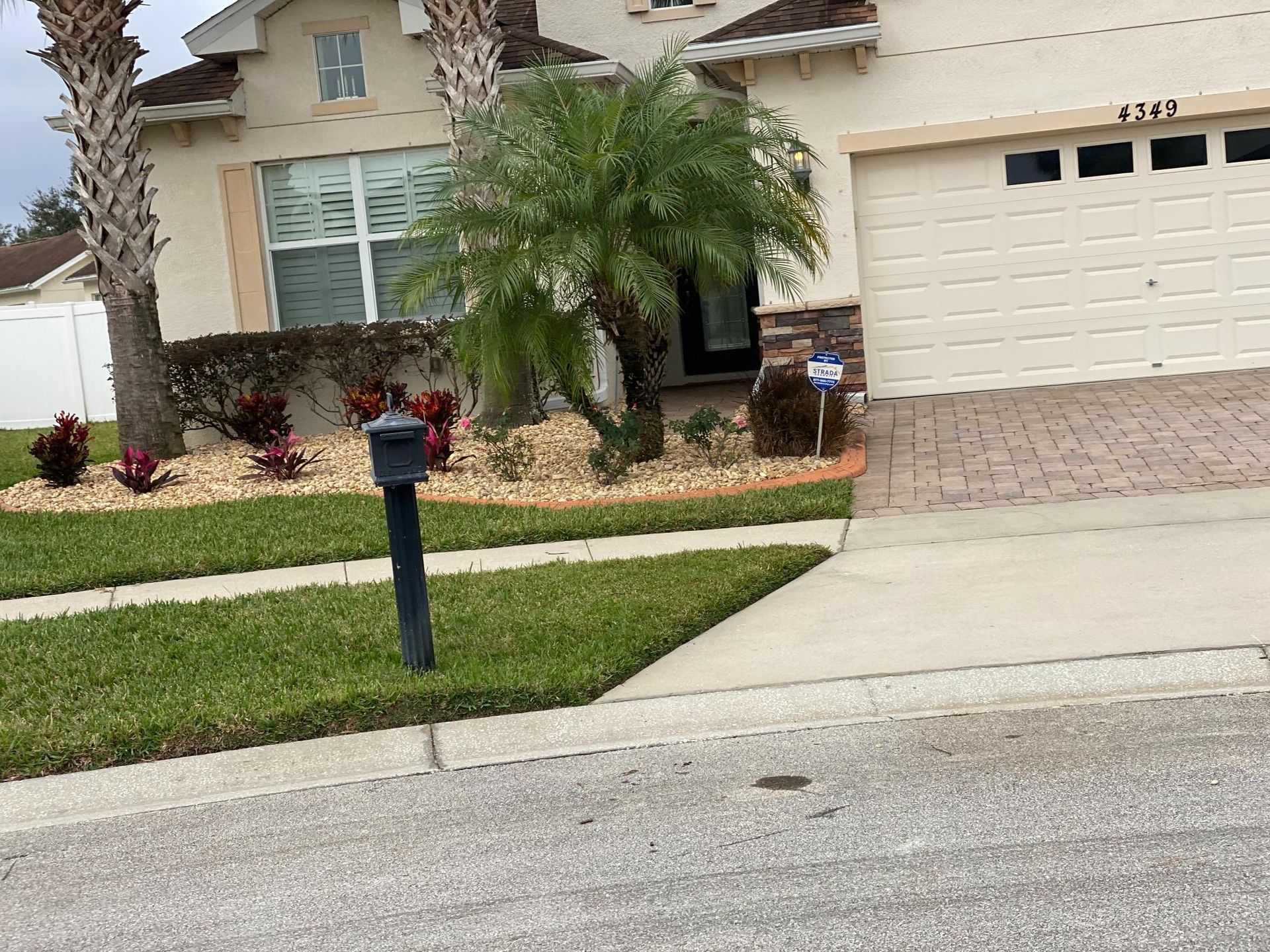 A beige house with a driveway and landscaping, including a palm tree and mailbox.