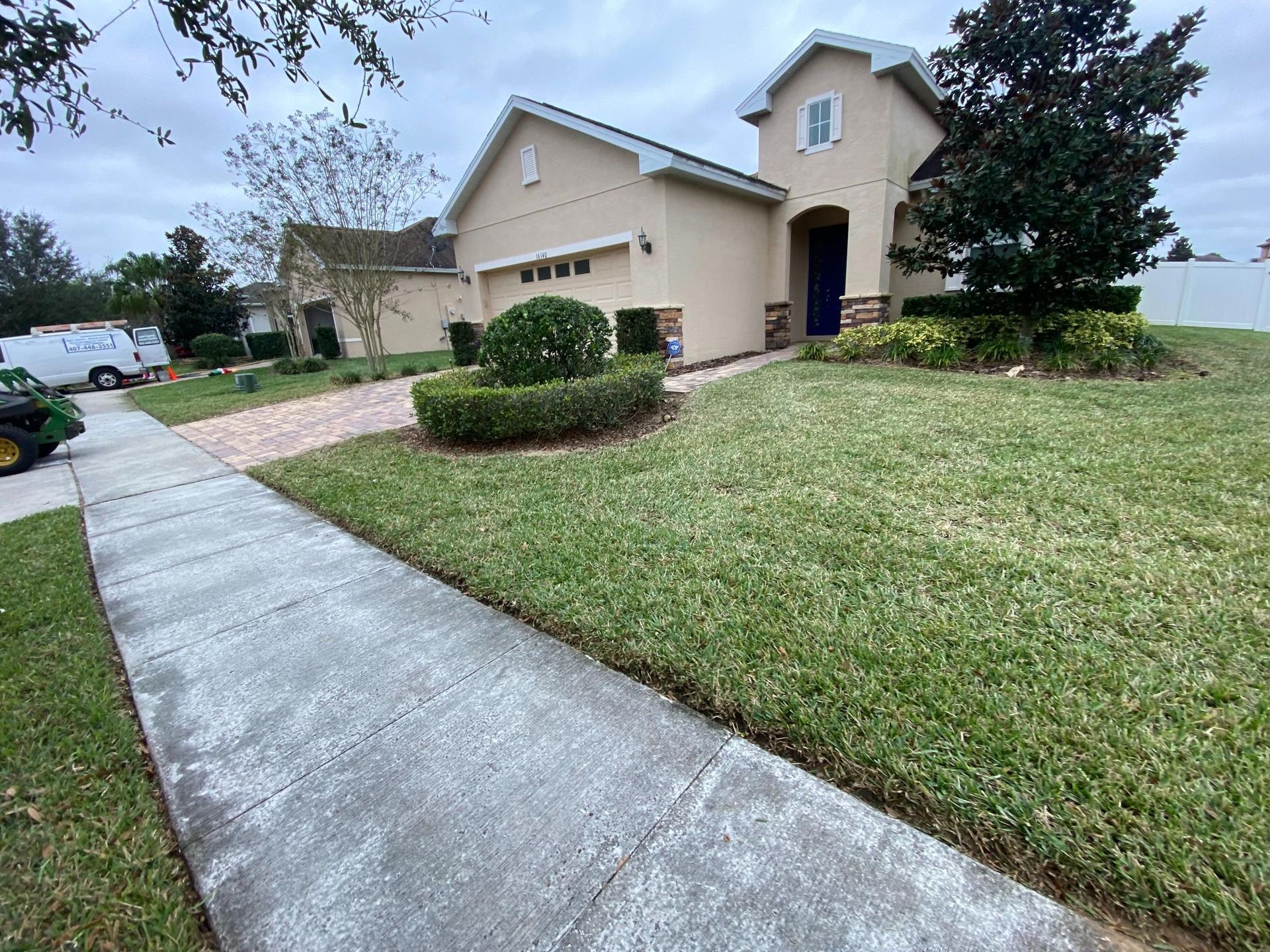 Beige house with a blue door, green lawn, sidewalk, and landscaping on a cloudy day.