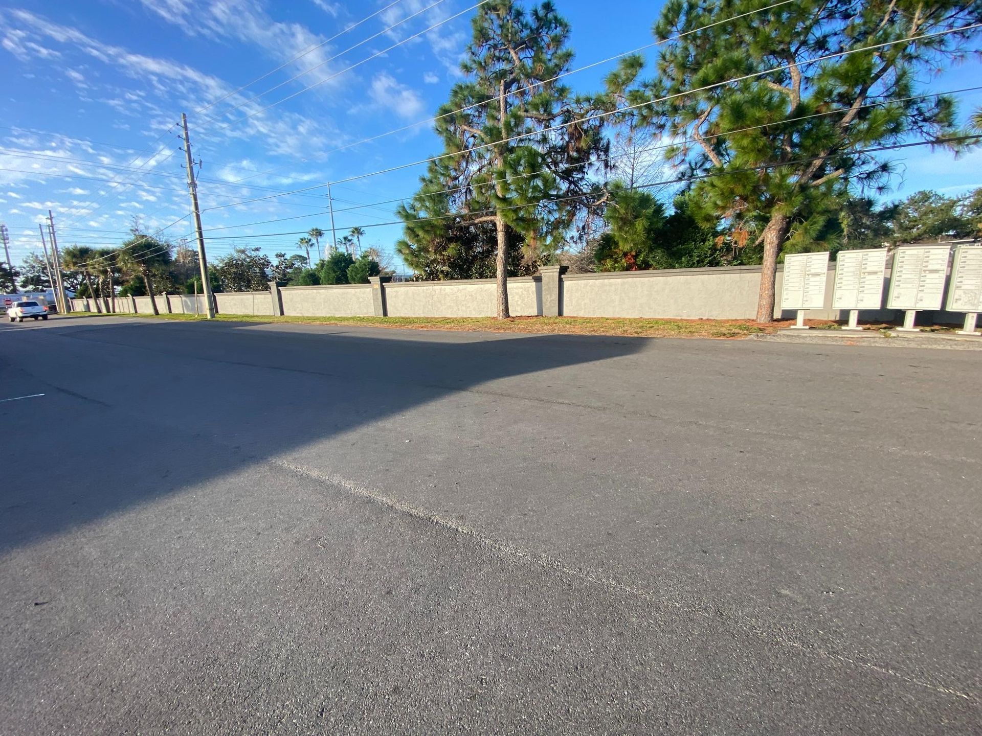 Asphalt road next to a concrete wall with trees and blue sky. A white car is visible.