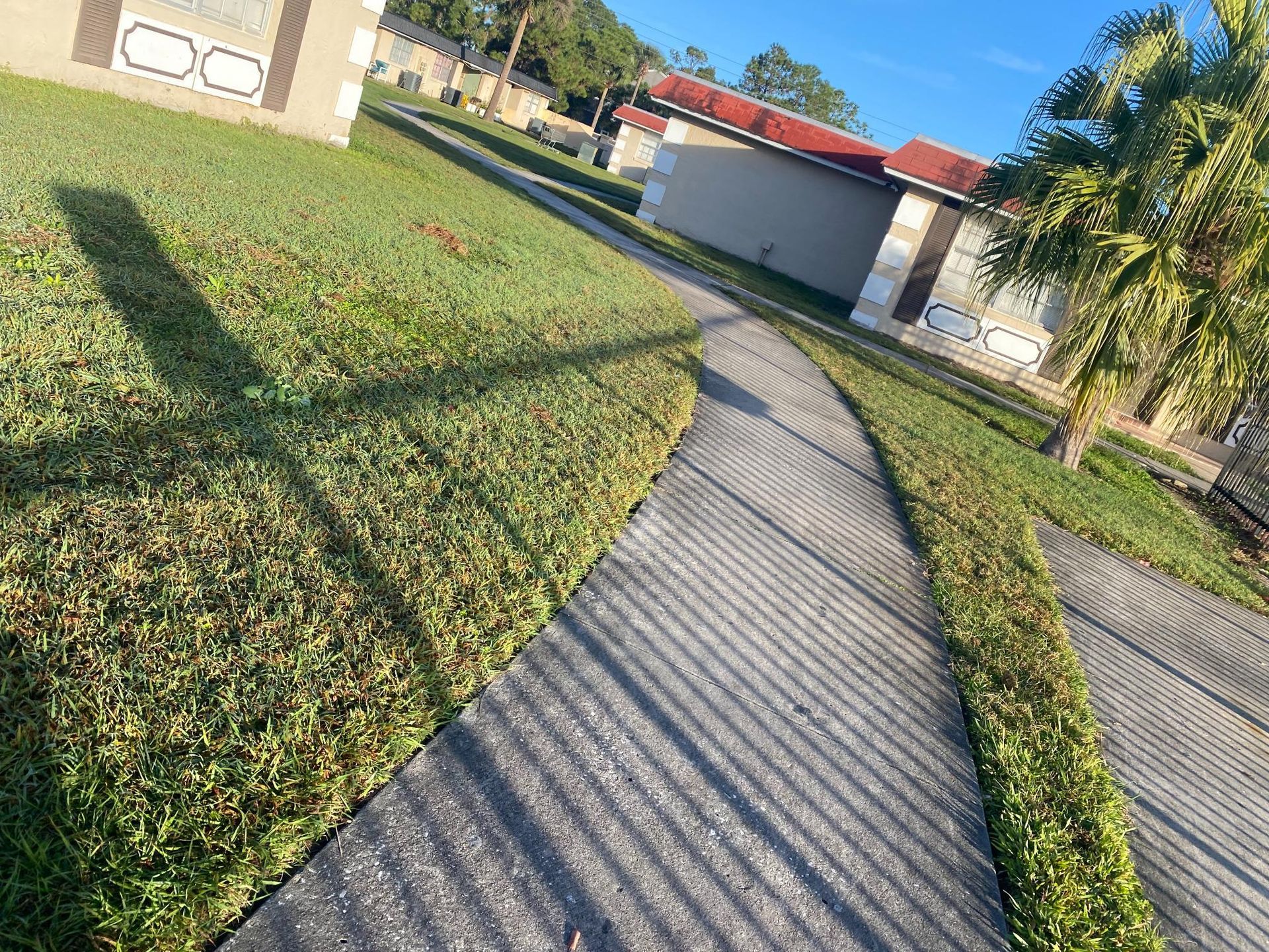 Pathway through green grass towards tan buildings with red roofs. Sunny day.