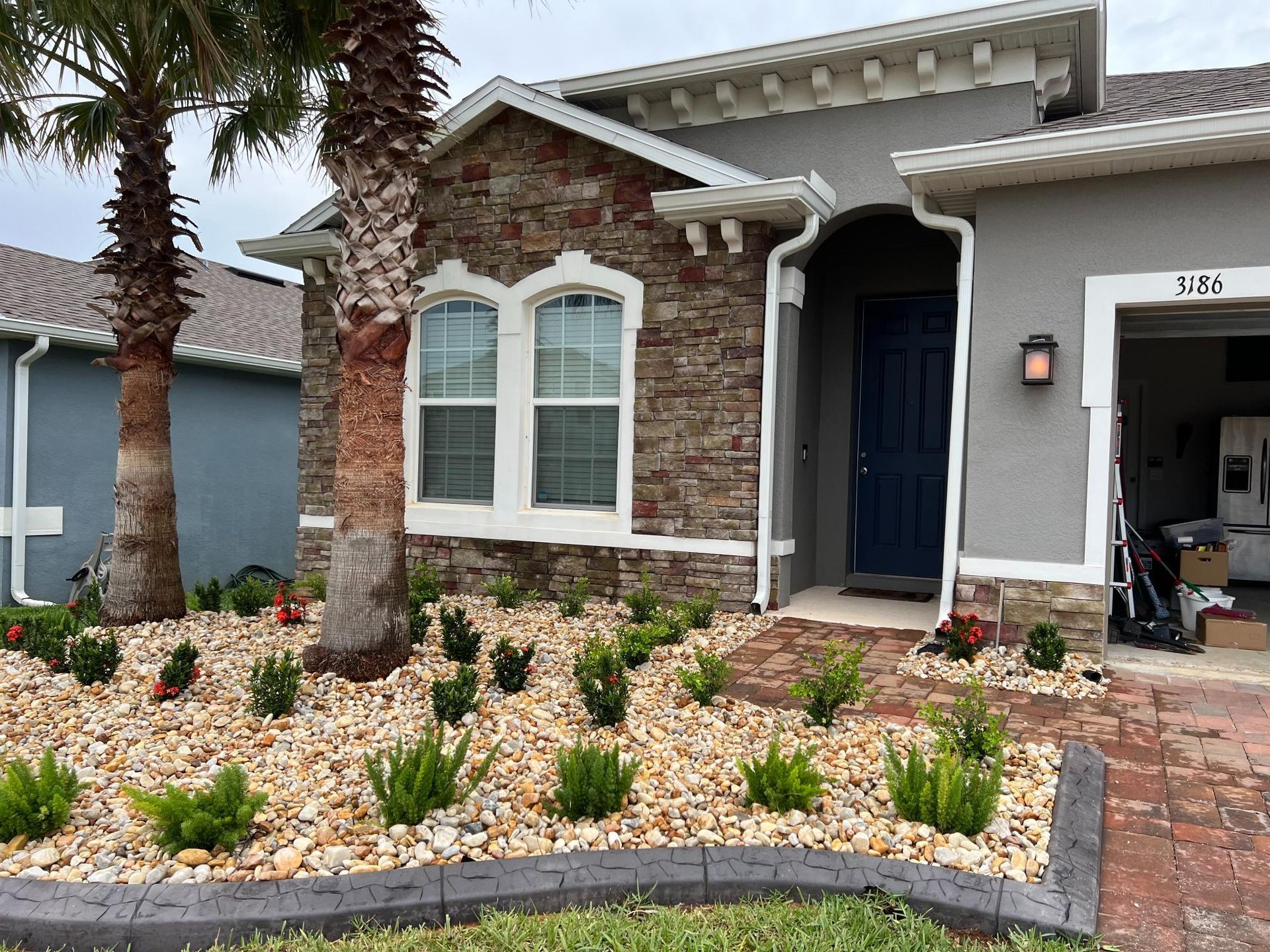 Front exterior of a house with stone accents, blue door, and landscaped yard with plants and rocks.