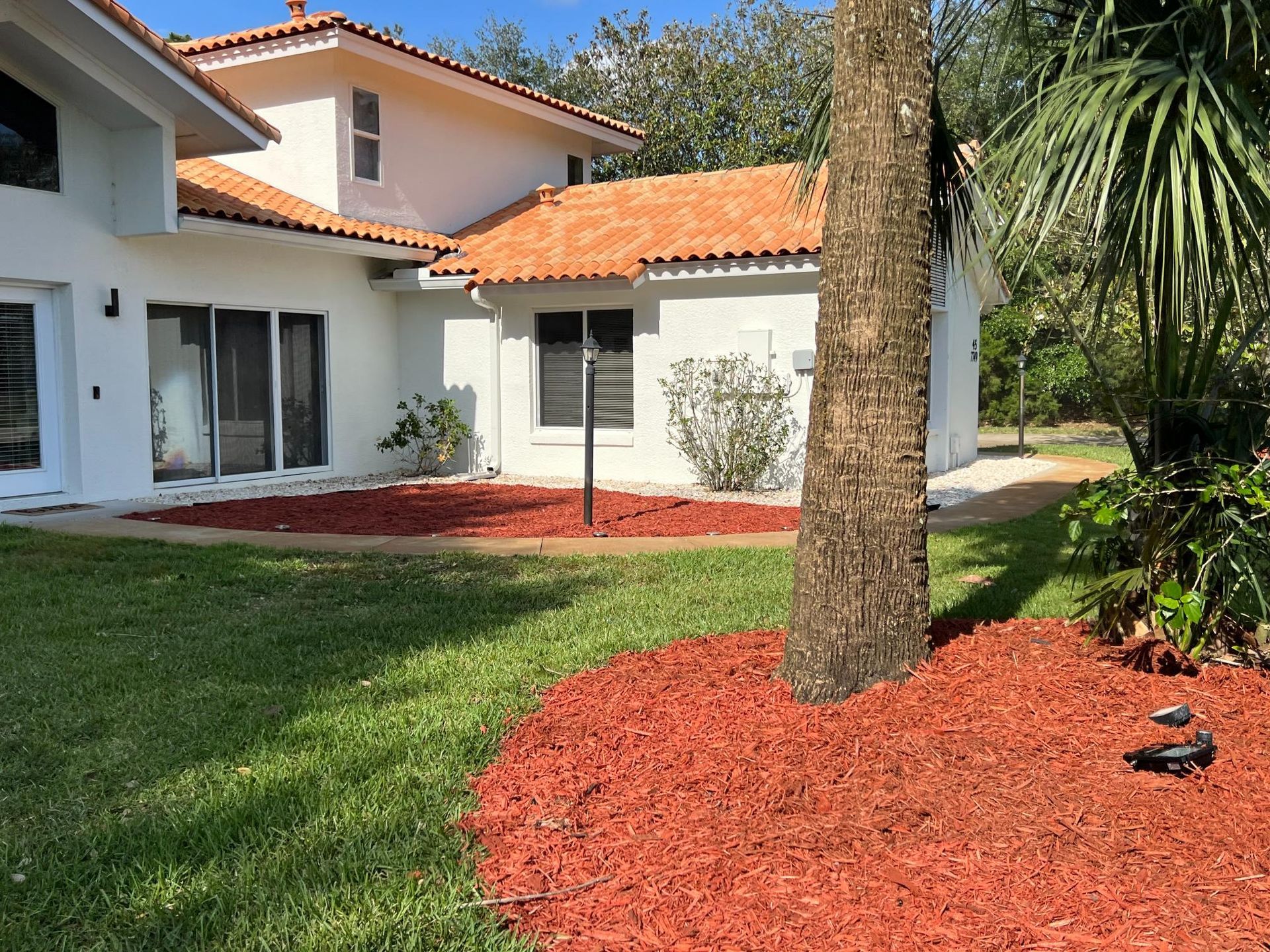 White house with a terracotta tile roof, red mulch in garden, and green grass.