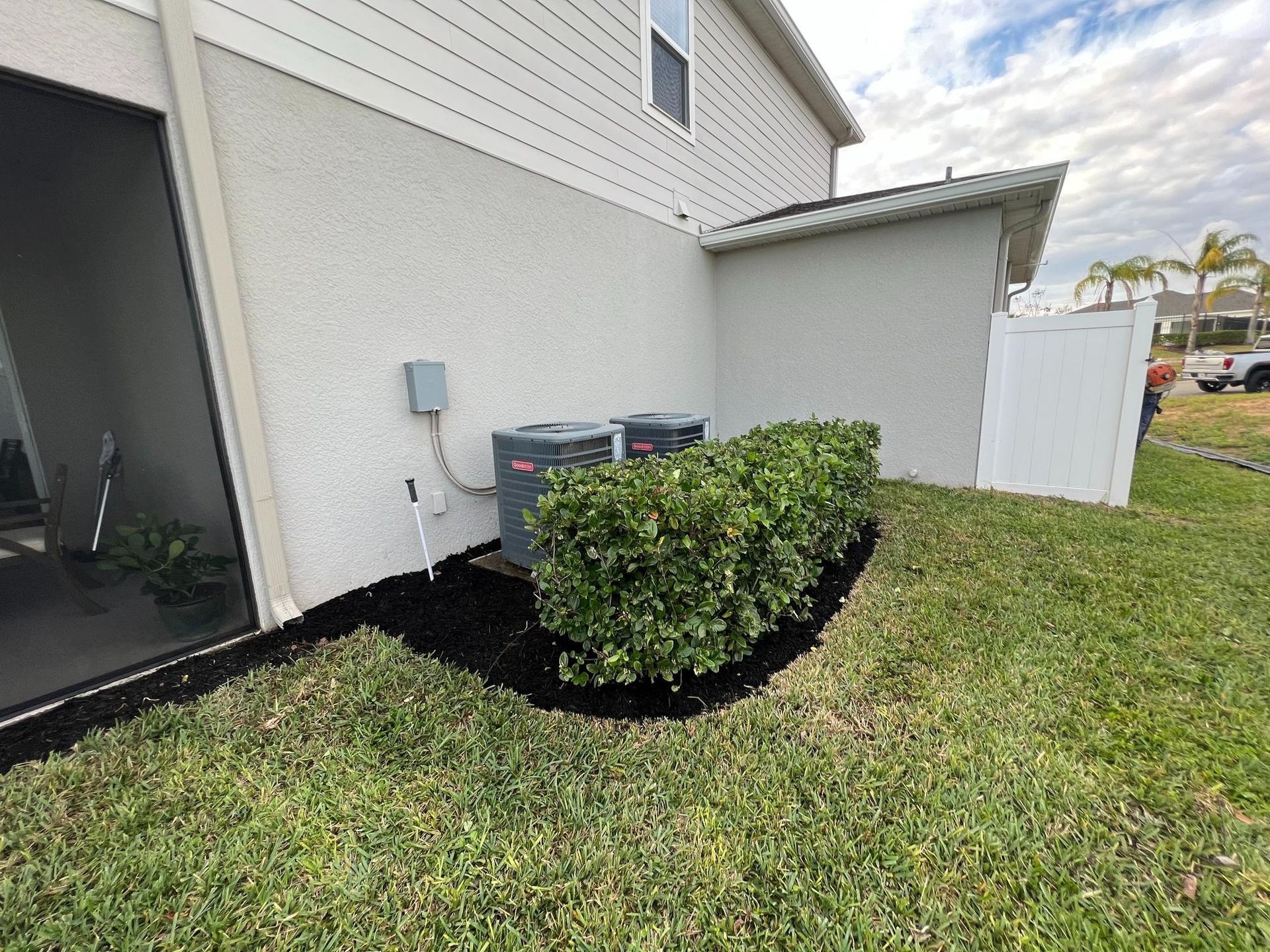 Backyard with HVAC units enclosed by green bushes and black mulch.