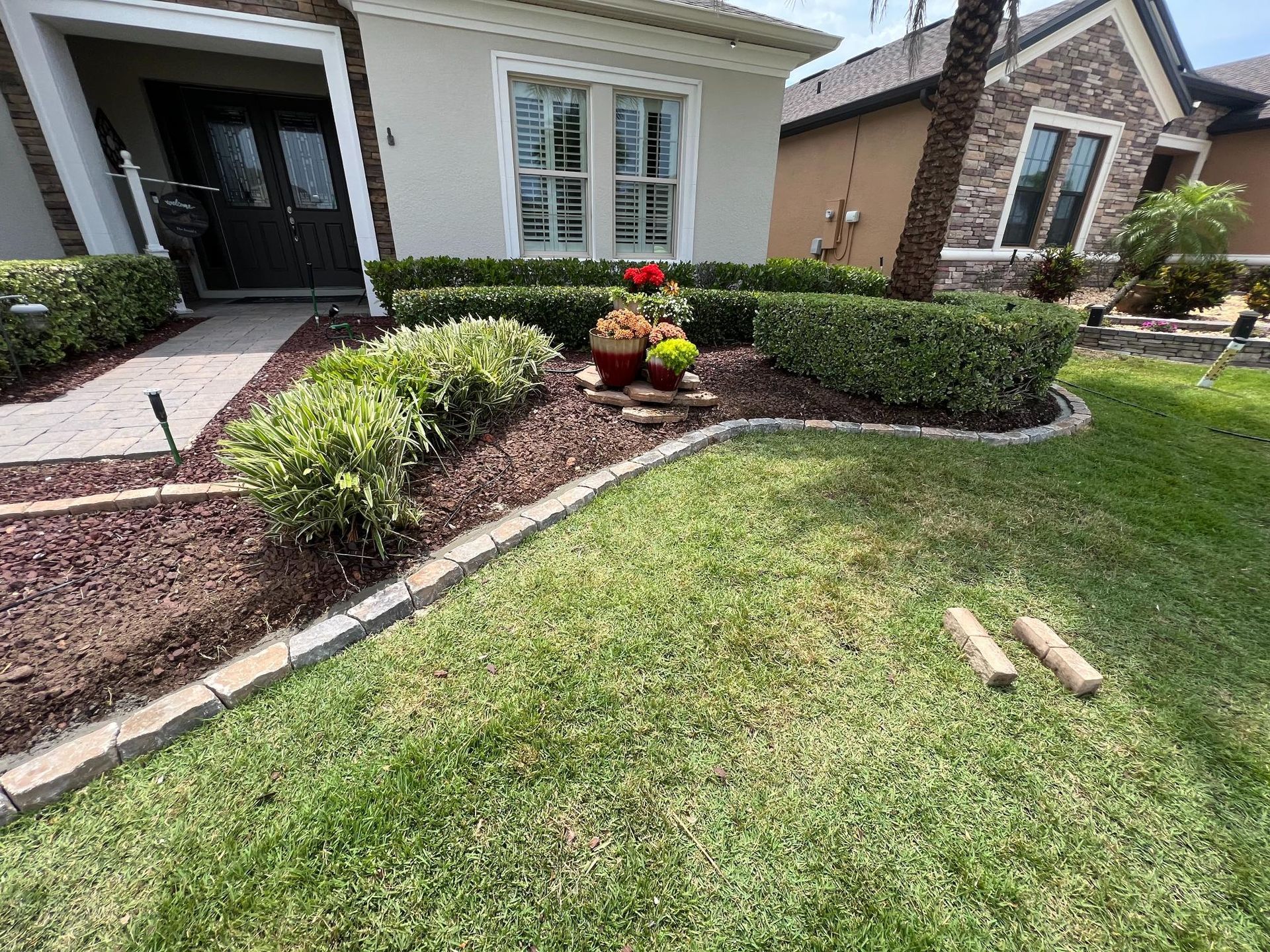 A house with manicured lawn and garden beds. Brown mulch, green hedges, and decorative flower pot near the front door.