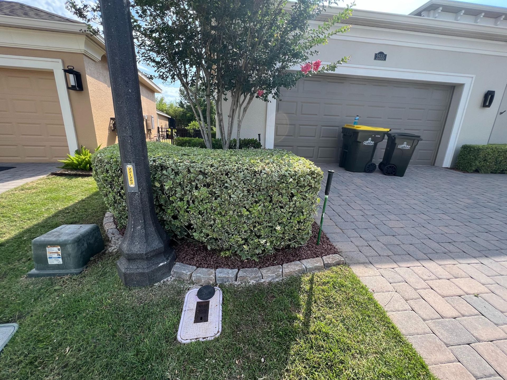 Lawn with a trimmed green bush, black lamp post, and a garage in a suburban setting.