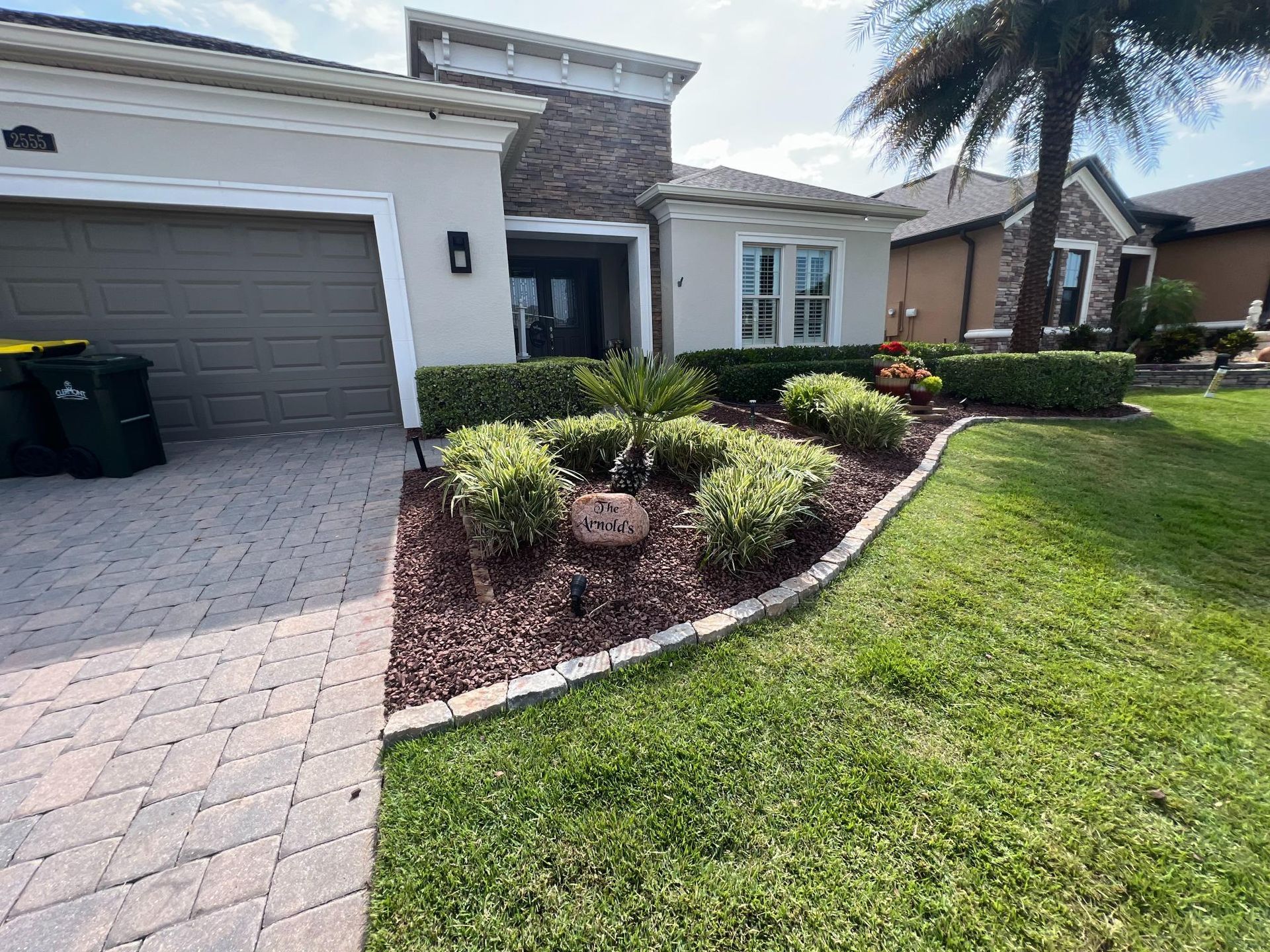 Exterior of a house with landscaped garden beds, green lawn, and a paved driveway.