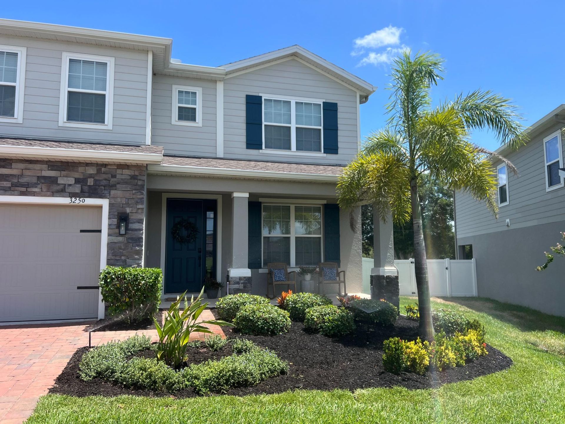 Two-story house with gray siding, blue shutters, and manicured landscaping.