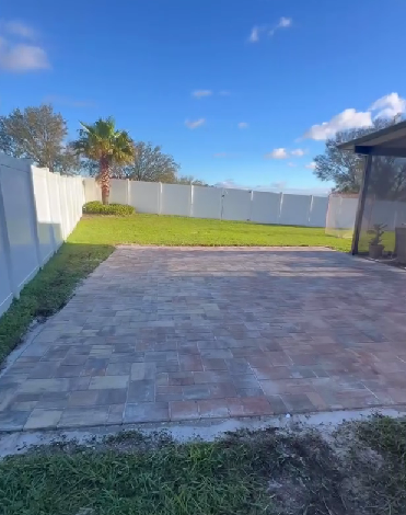 Patio with brick pavers, lawn, white fence, palm tree, and clear blue sky.