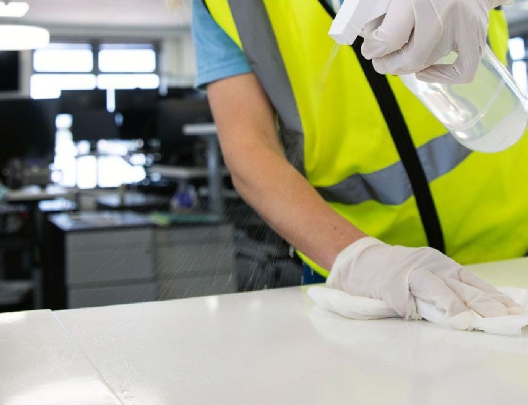 Une personne en gilet jaune nettoie un comptoir avec un vaporisateur désinfectant chez push push propreté