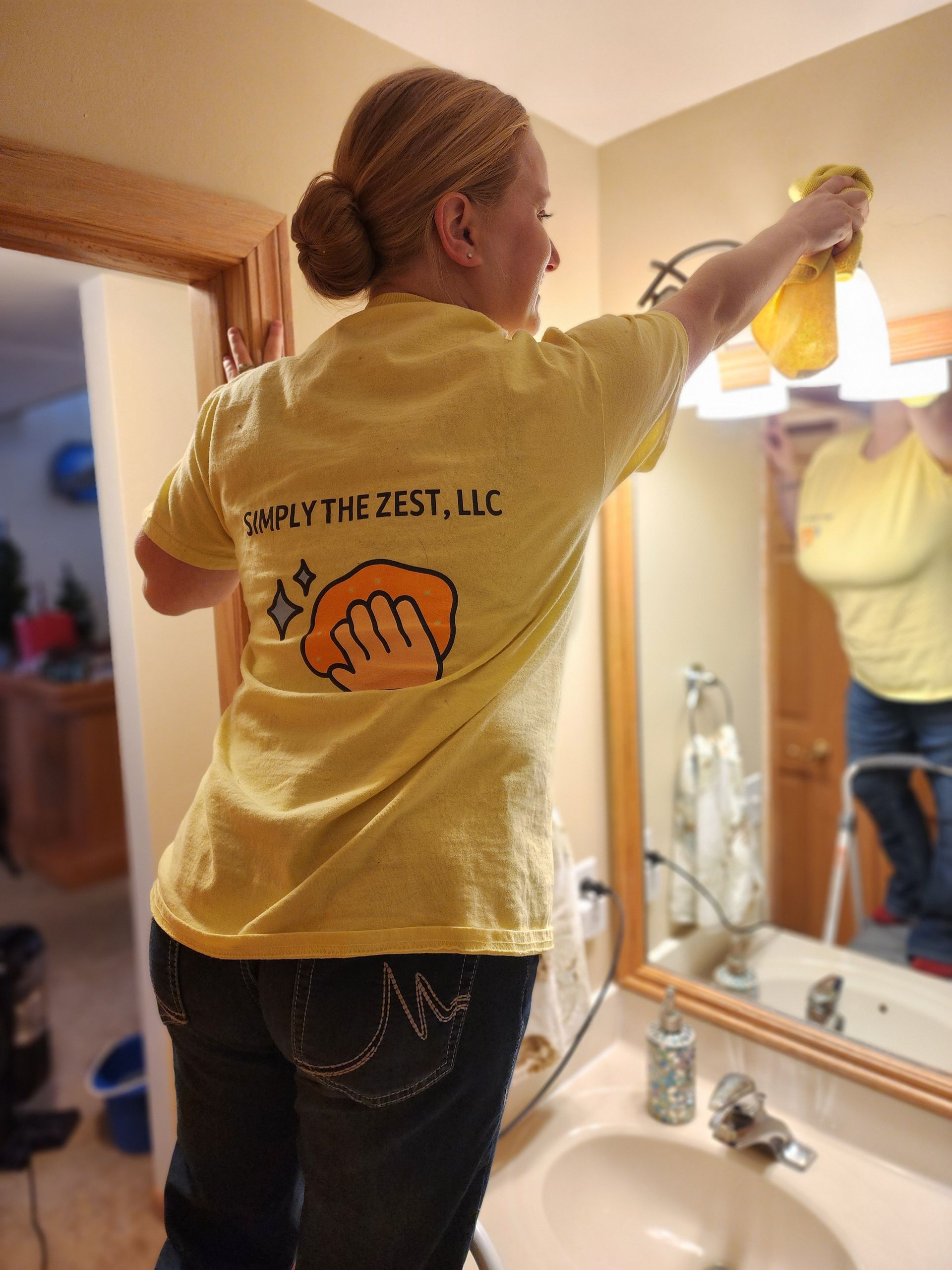 Woman in yellow shirt cleaning bathroom light fixture. 