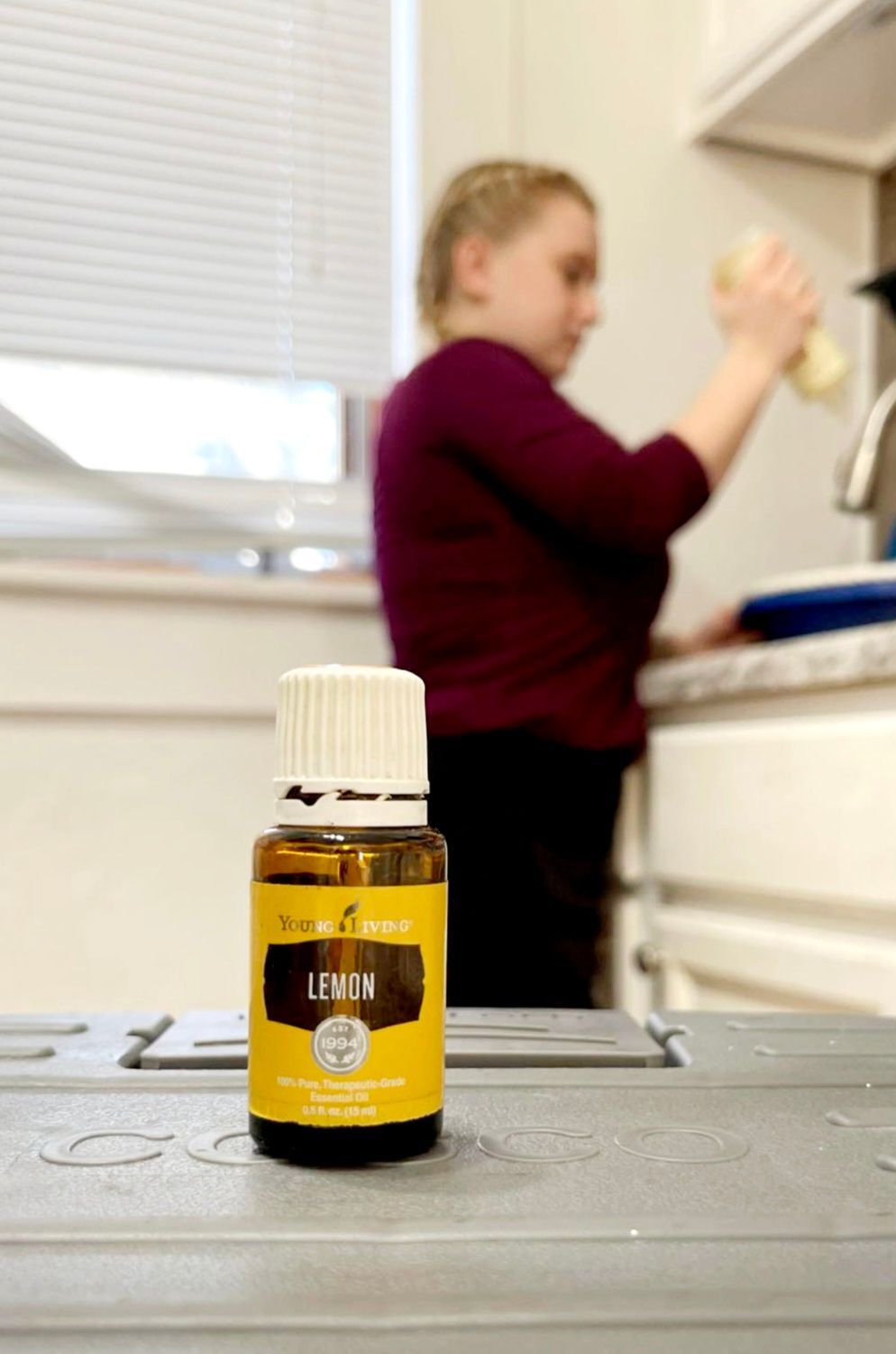 Bottle of Young Living Lemon essential oil, with a person in the background at a sink.