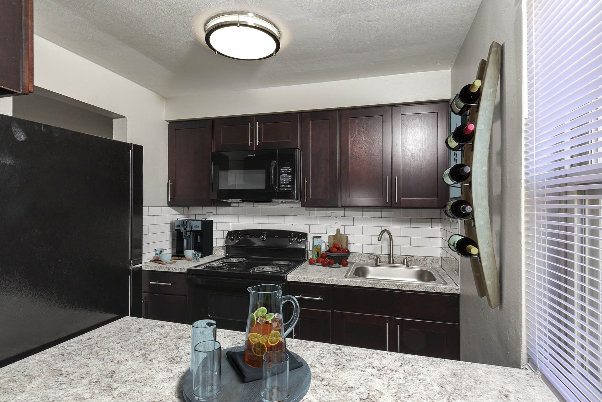 Kitchen in an apartment with dark wood cabinets, black appliances, and a sink by a window at The Alden South Hills in Pittsburgh, PA. 