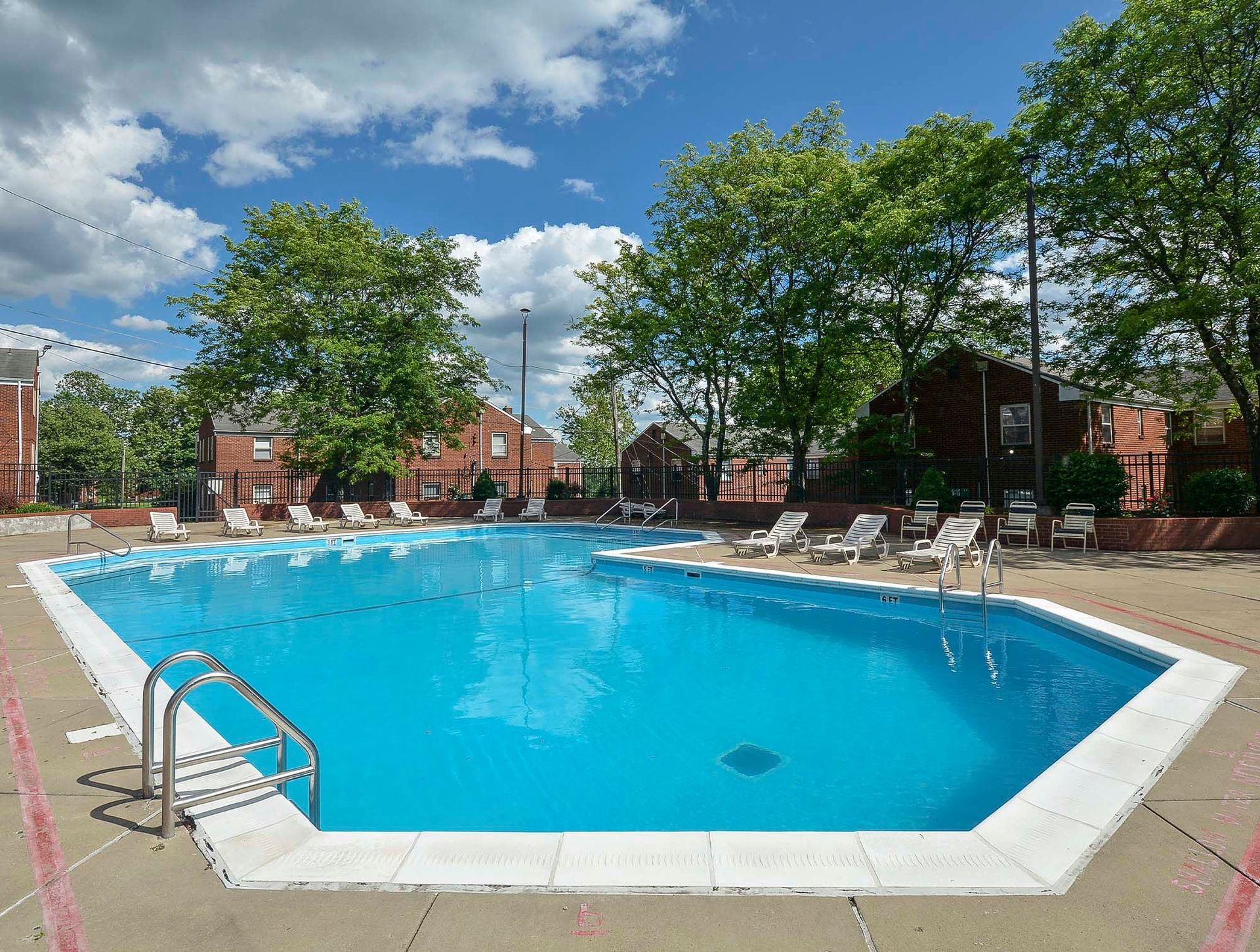 Outdoor community pool with lounge chairs, surrounded by trees and brick buildings at The Alden South Hills in Pittsburgh, PA. 