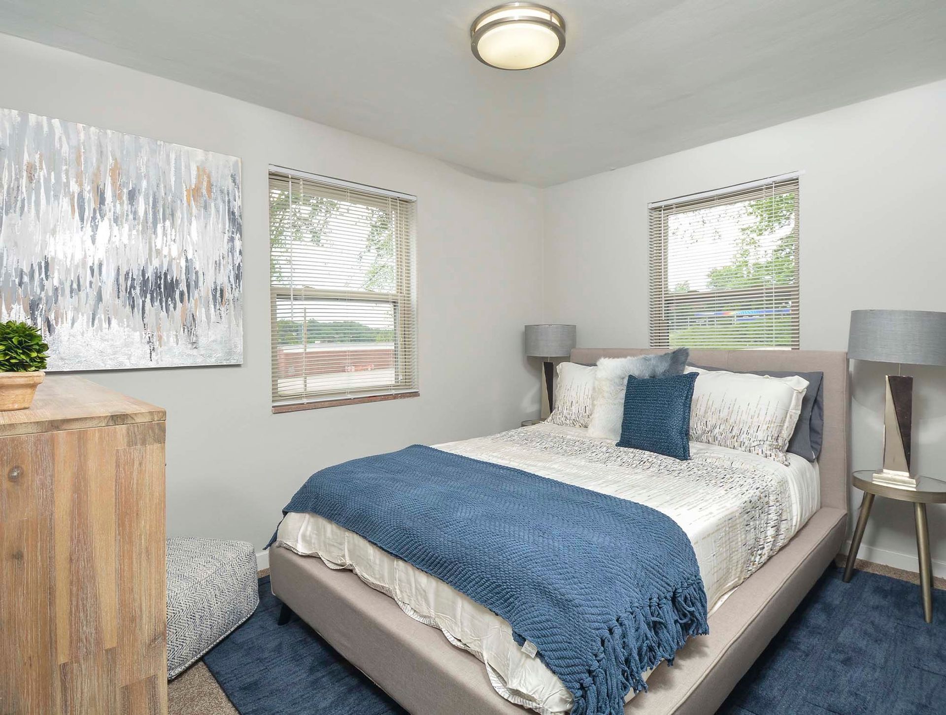 Furnished apartment bedroom with a bed, dresser, two nightstands, and blinds on two windows at The Alden South Hills in Pittsburgh, PA. 