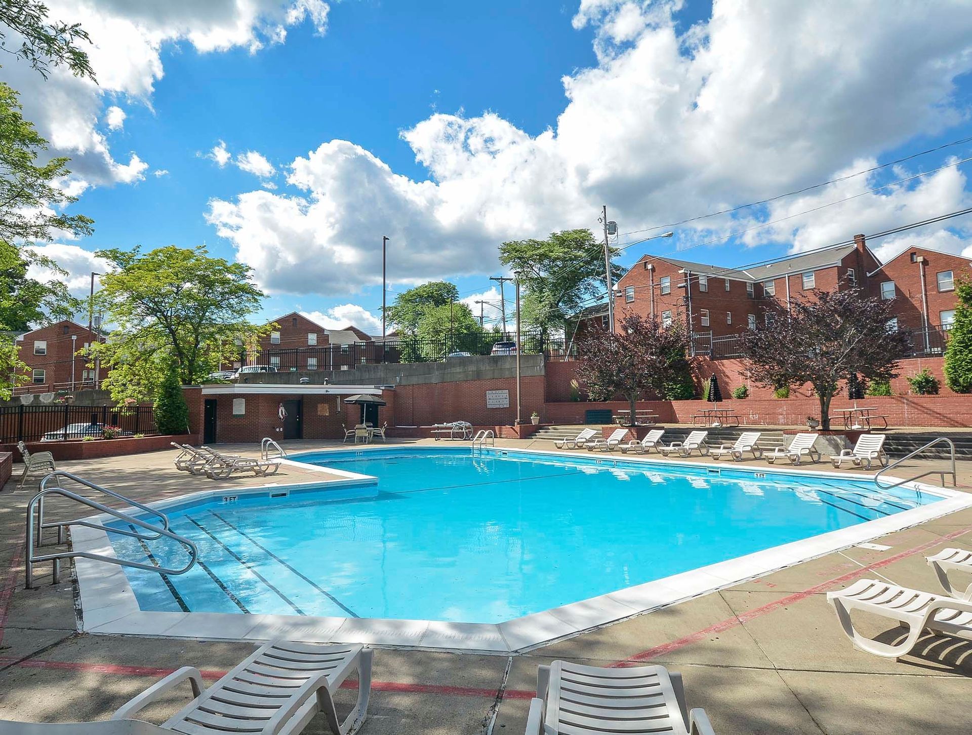 Outdoor pool at a multifamily community with lounge chairs and brick buildings under a blue sky at The Alden South Hills in Pittsburgh, PA. 