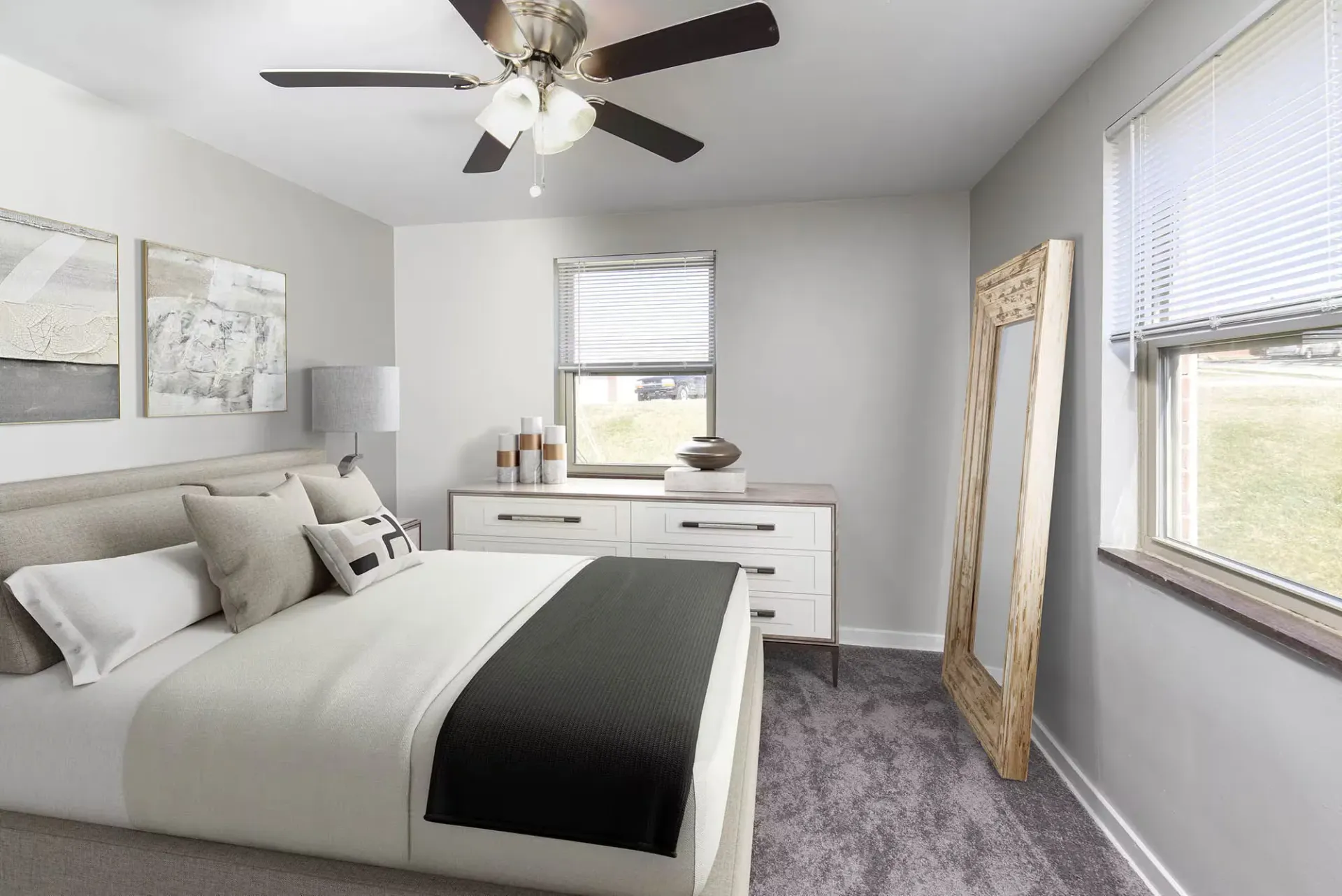 Bedroom in a modern apartment with a bed, dresser, and a leaning floor mirror at The Alden South Hills in Pittsburgh, PA. 