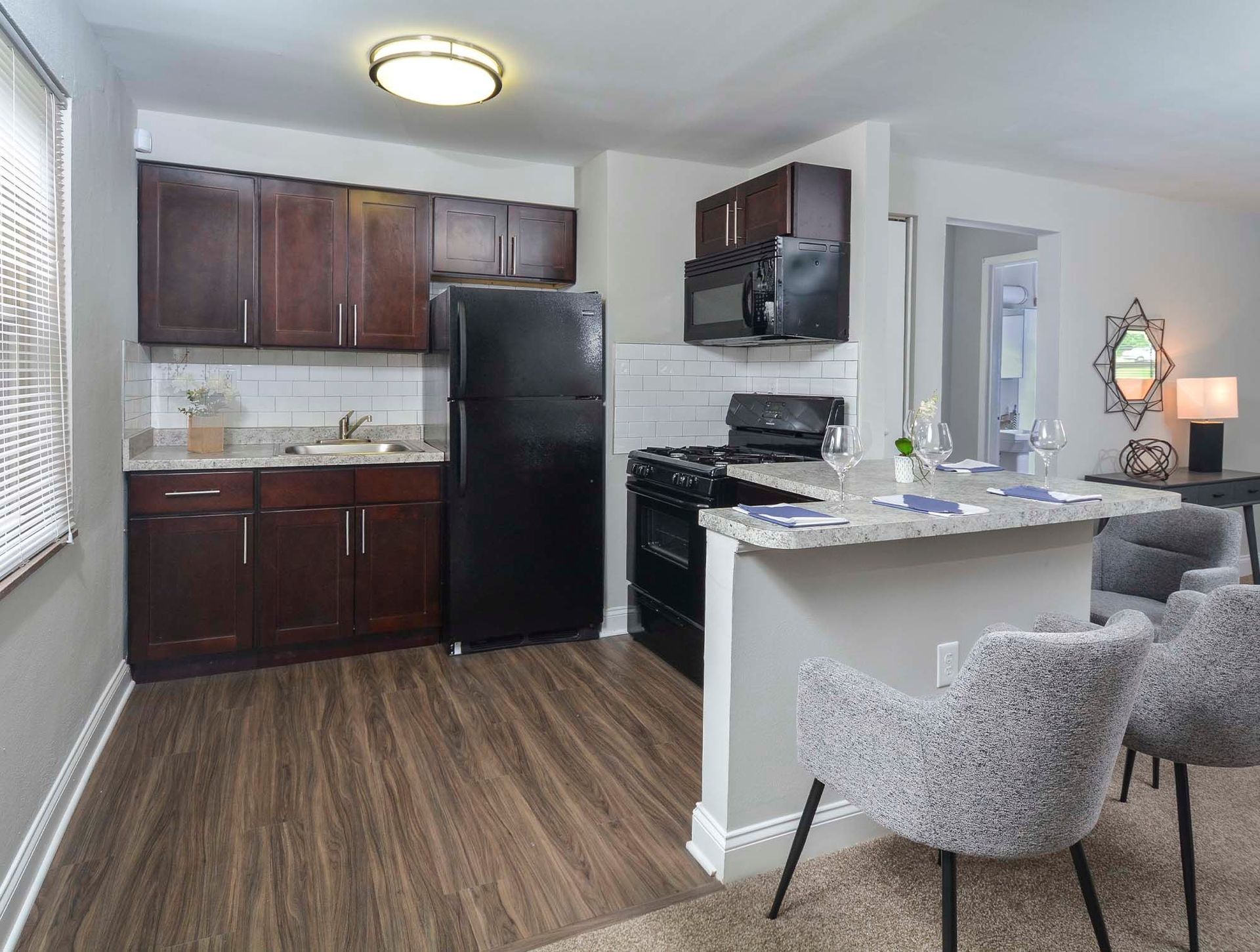 Kitchen with dark wood cabinets, black appliances, and a granite island with seating at The Alden South Hills in Pittsburgh, PA. 
