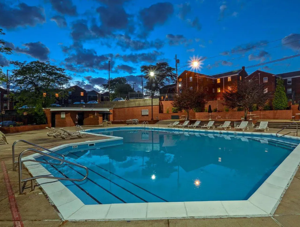 Outdoor apartment community pool at dusk with lounge chairs and brick buildings in background at The Alden South Hills in Pittsburgh, PA. 