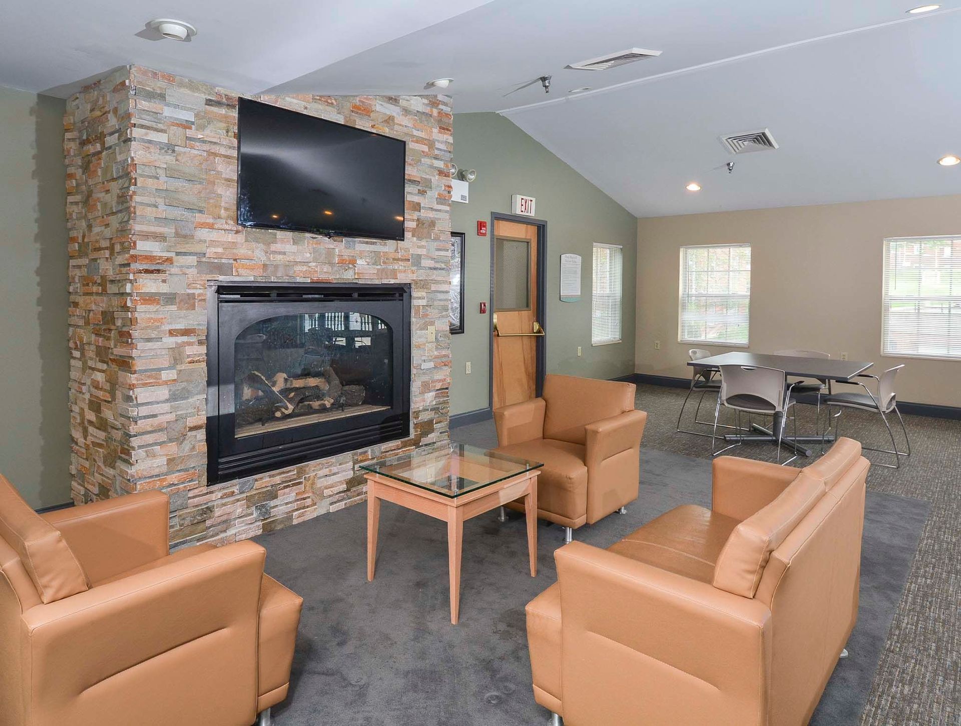 Common lounge area with a stone fireplace, wall-mounted TV, and tan seating at The Alden South Hills in Pittsburgh, PA. 