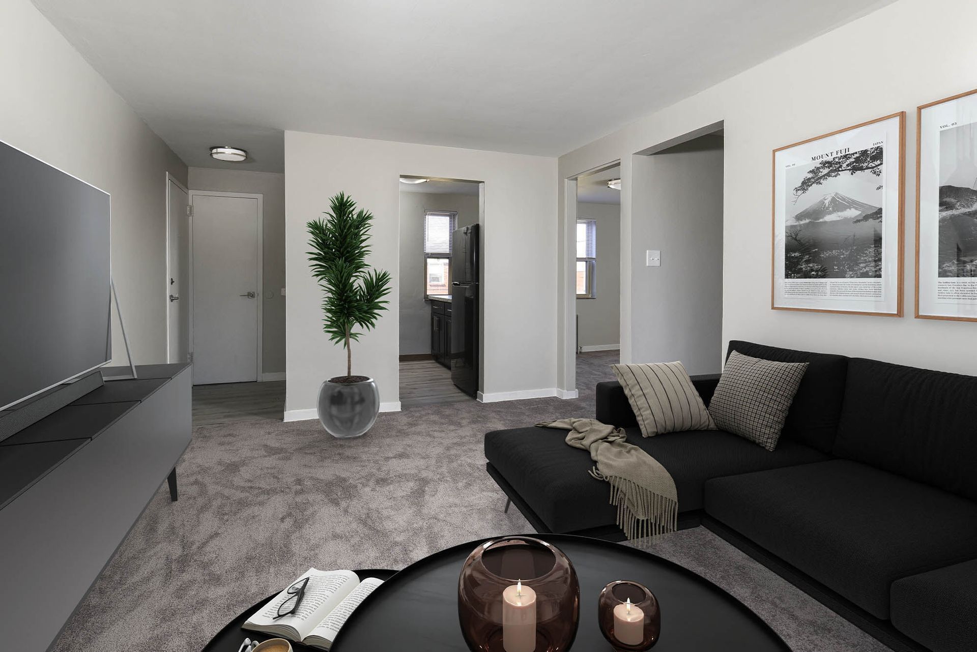 Living room in a modern apartment with a black sectional sofa, round coffee table, TV, and a potted plant at The Alden South Hills in Pittsburgh, PA. 