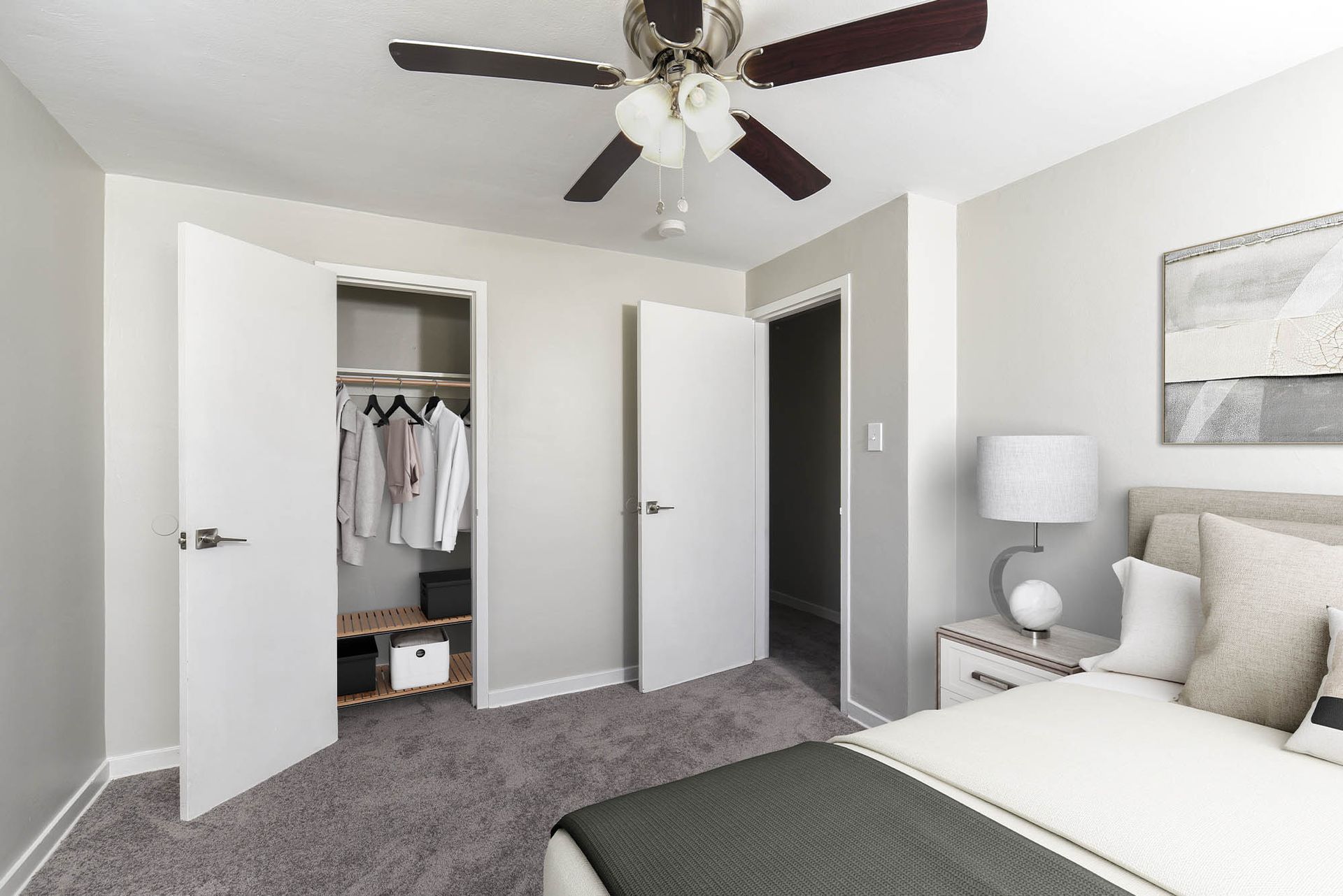 Bedroom interior with a bed, nightstand, ceiling fan, and an open closet at The Alden South Hills in Pittsburgh, PA. 