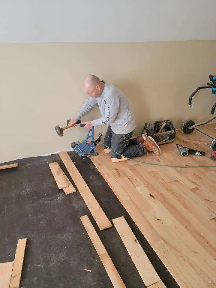 A man is kneeling on the floor holding a hammer.