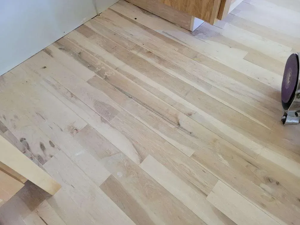 A close up of a wooden floor with a vacuum cleaner in the background.