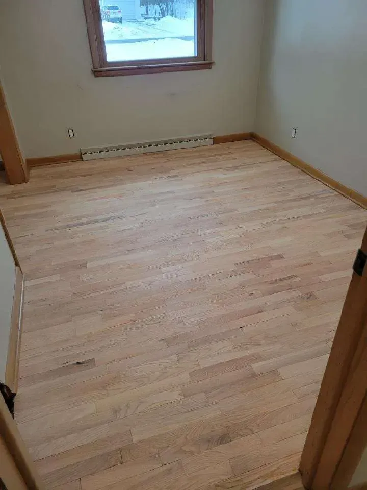 A bedroom with hardwood floors and a window.