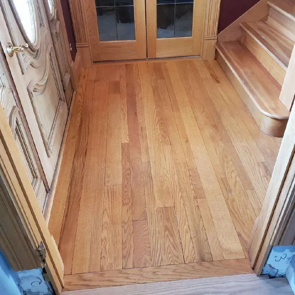 A hallway with hardwood floors and stairs in the background