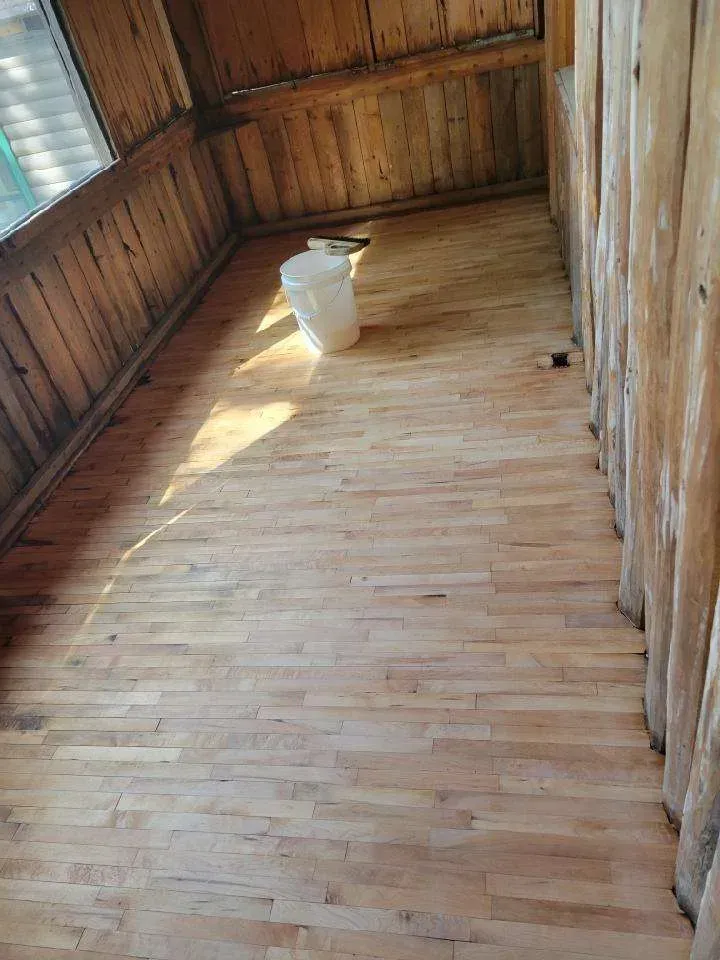 A wooden floor in a room with a bucket on it.