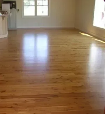 A living room with hardwood floors and a kitchen in the background.