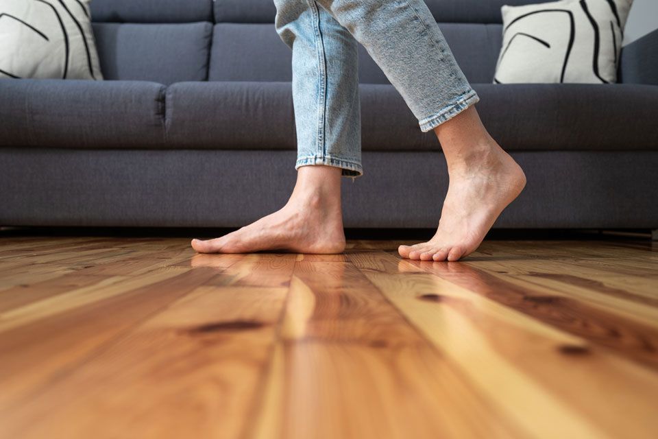 A person is walking barefoot on a wooden floor in a living room.