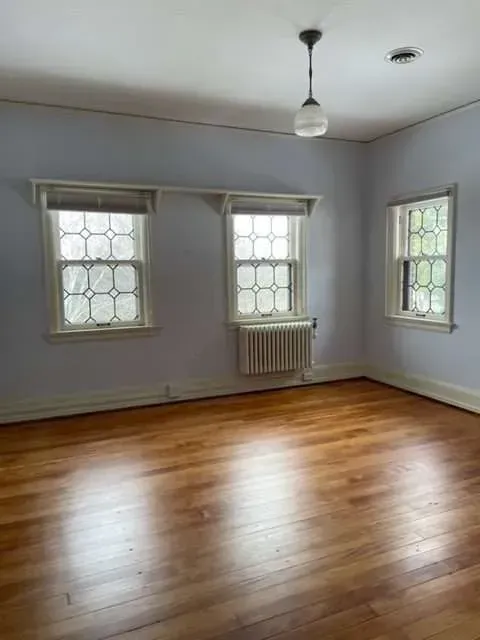 An empty room with hardwood floors and three windows.