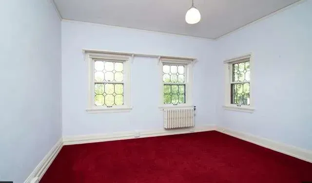 An empty room with a red carpet and two windows
