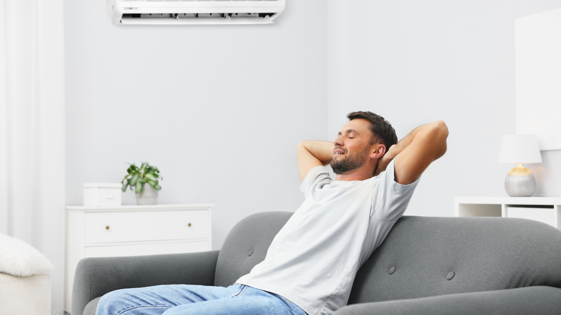 Man relaxes on a sofa under an air conditioner in a living room.
