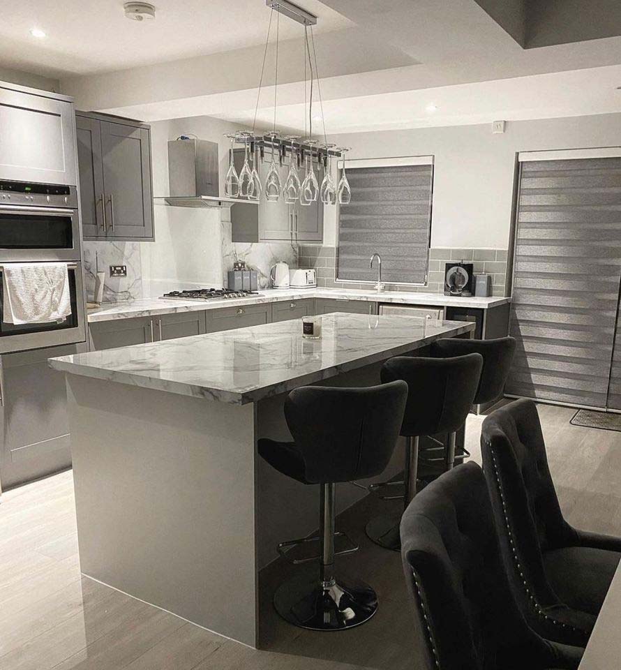 A modern grey kitchen with grey blinds and lots of black chairs