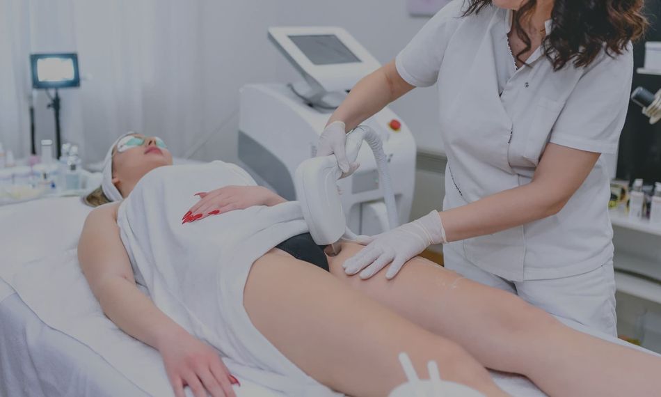 Woman receiving laser hair removal treatment on legs in clinic.