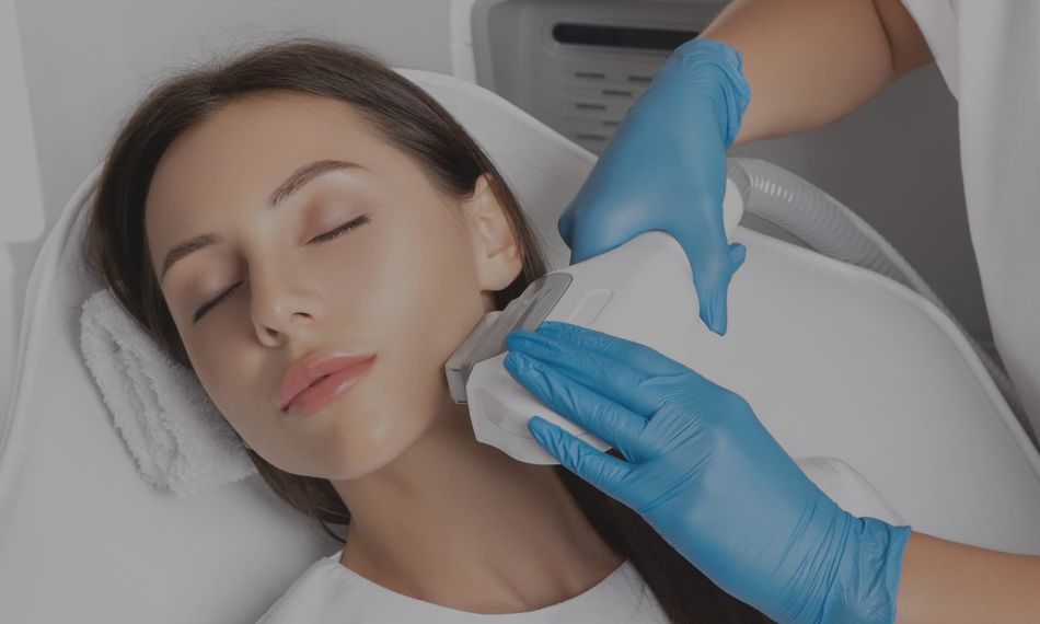 Woman receiving facial treatment; technician using a handheld device on her jawline.