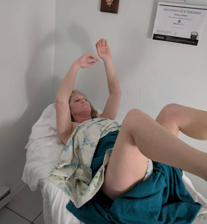 Woman lying on a massage table, arms raised, wrapped in a blanket.