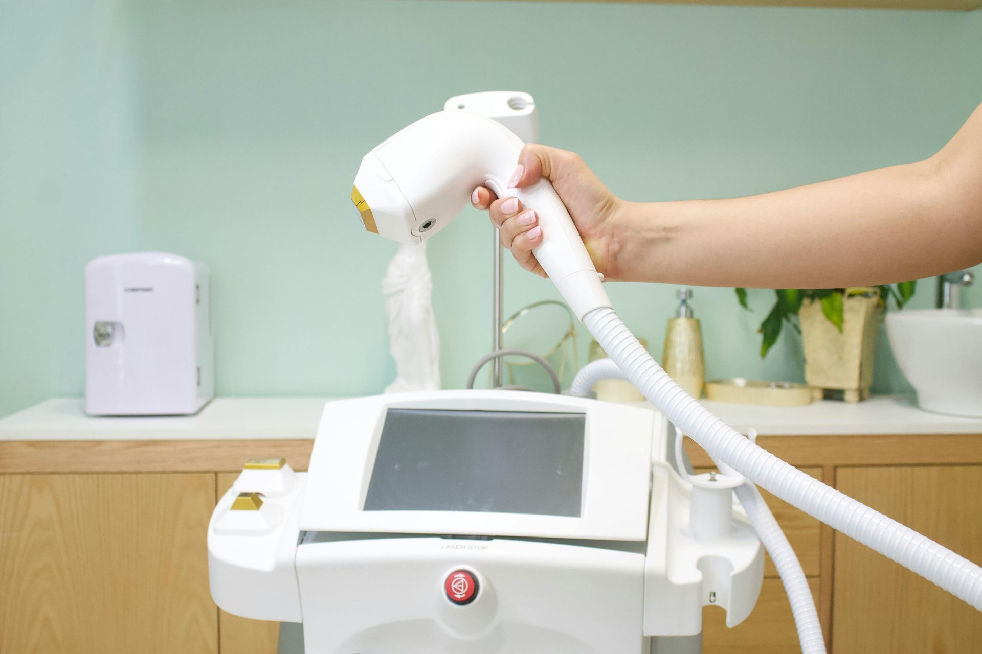 Hand holding a laser hair removal device. White machine in a salon setting.
