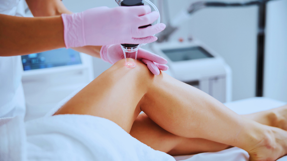 Person in pink gloves performing laser treatment on a leg.