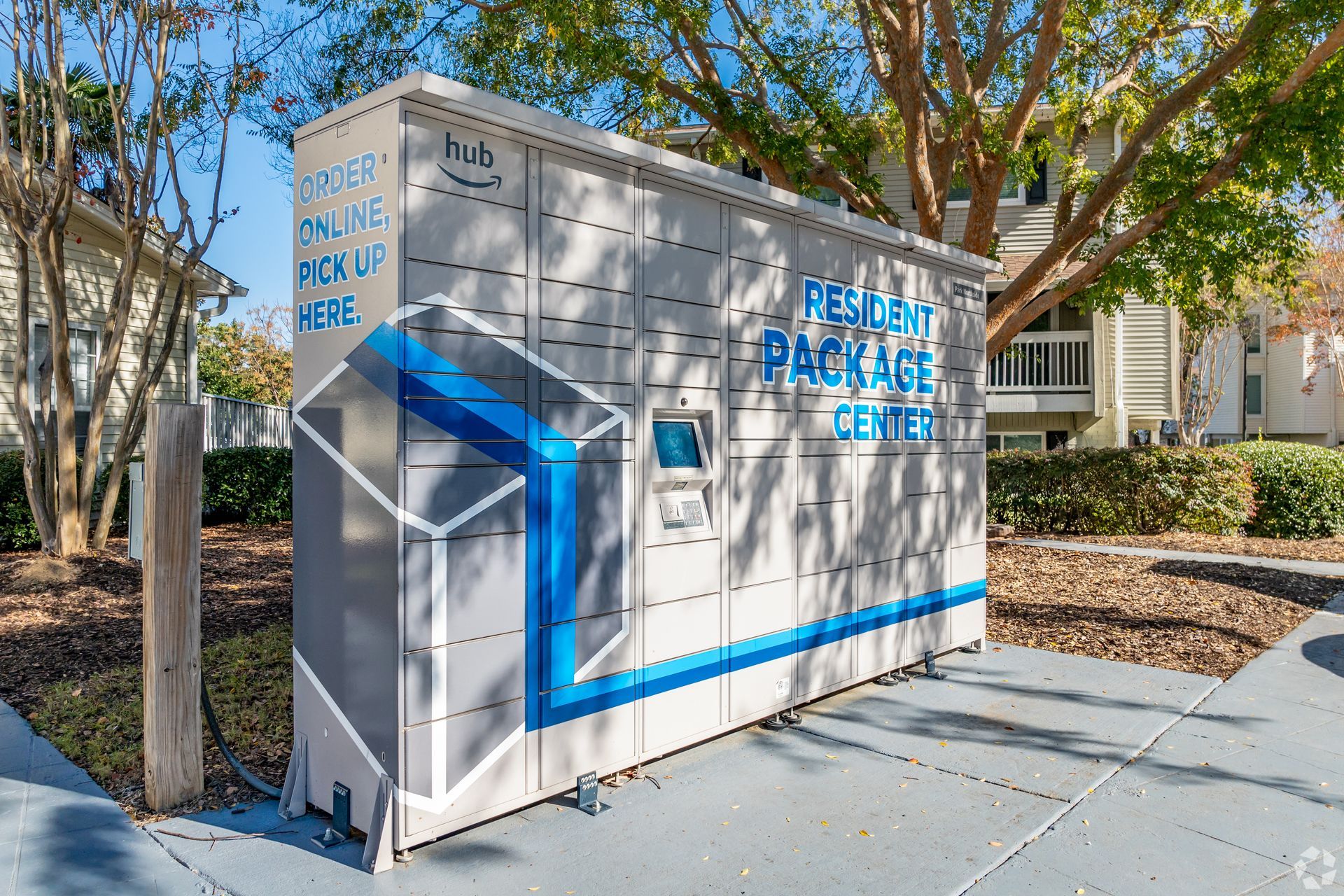 A grey and blue Amazon Hub parcel locker stationed outdoors in a residential complex setting.