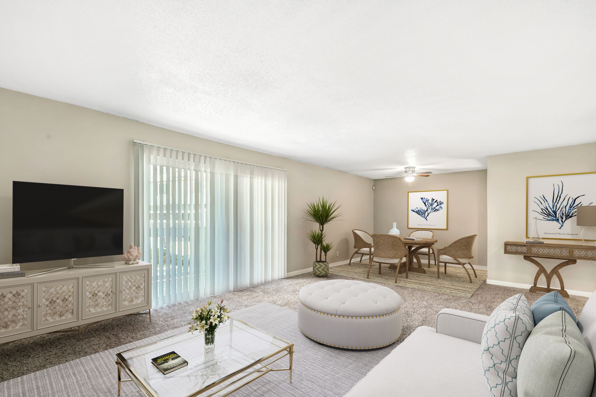 A light-colored living room with a TV, a white circular ottoman, and a dining area with a table and four wicker chairs.