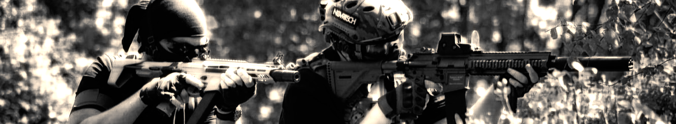 Two soldiers in tactical gear aiming rifles in a forested environment. Black and white.