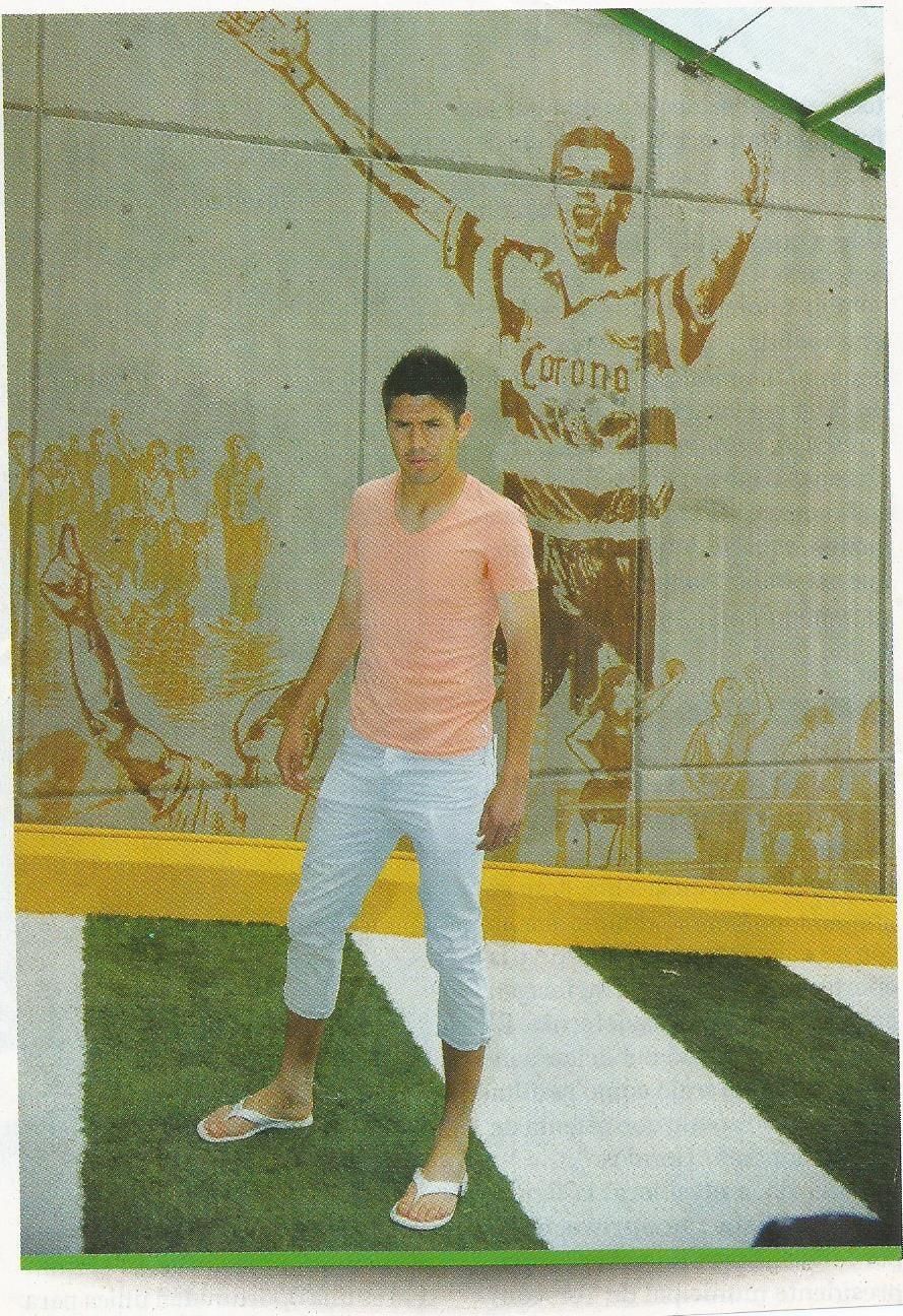 Un hombre con una camisa rosa y pantalones blancos está parado frente a un mural de un hombre que lleva una camiseta de corona.