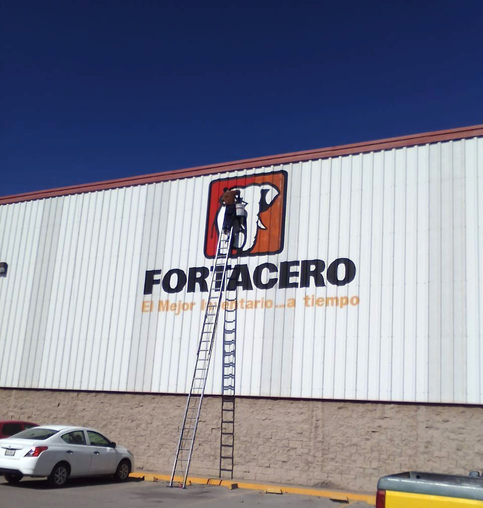 Un hombre en una escalera está pintando un cartel para Fortacero.