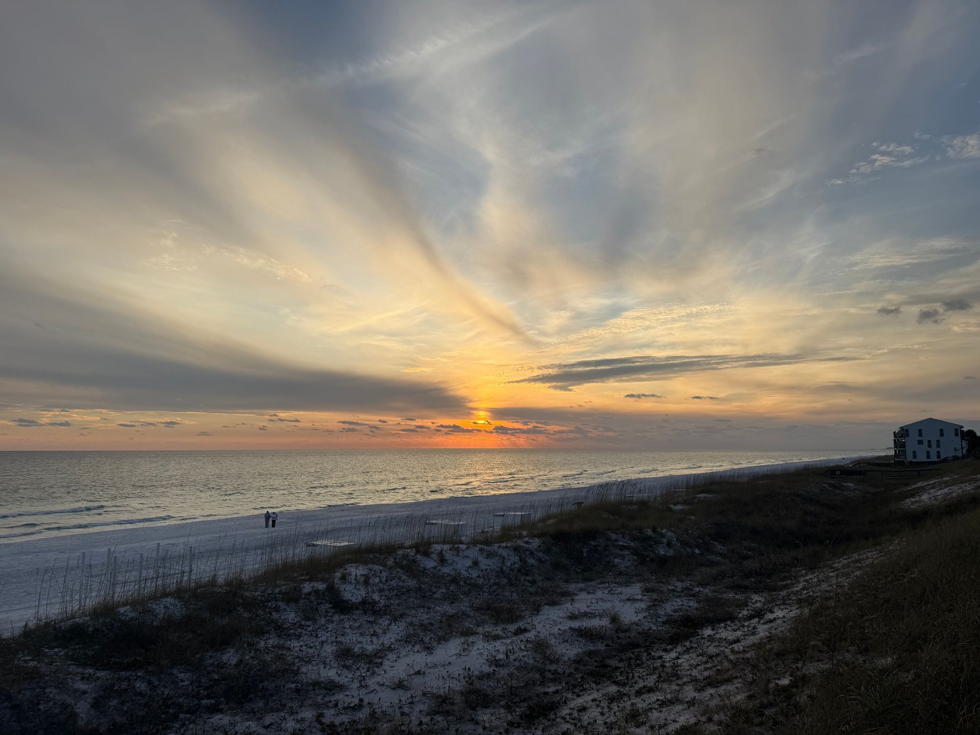 A sunset over the ocean with a house in the distance.