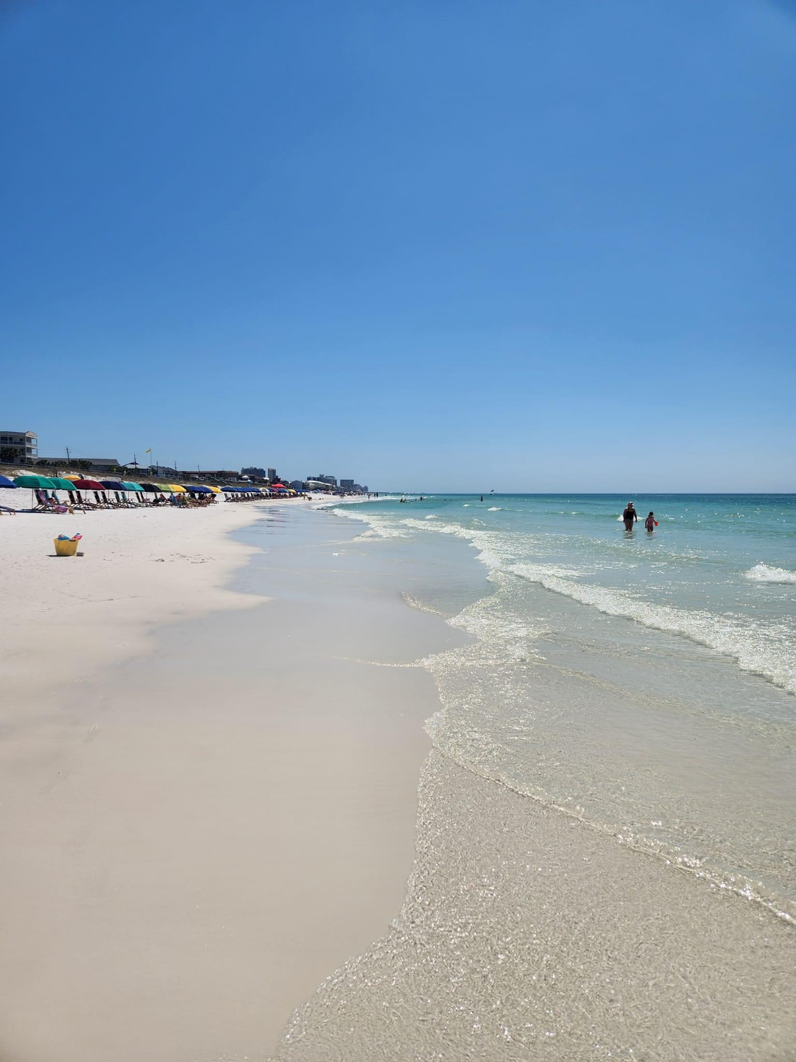 A beach with a lot of umbrellas and people swimming in the ocean.